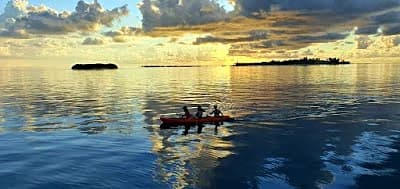 Sunset cruise boat on calm Maldives ocean waters near a resort island at dusk